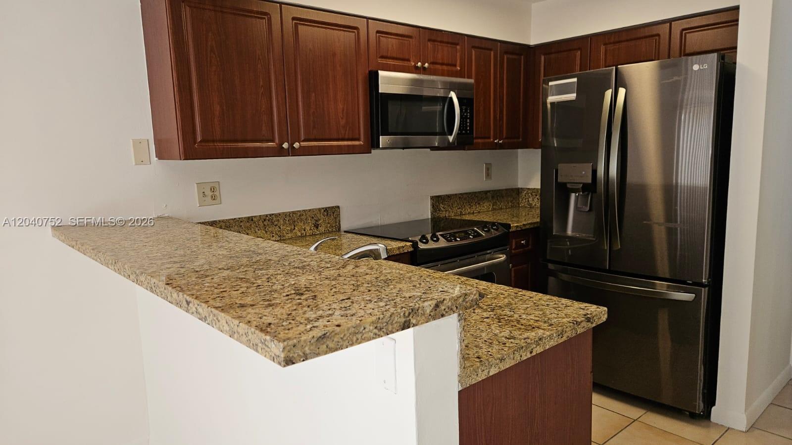 A kitchen features dark wood cabinets, granite countertops, and stainless steel appliances — 8460 SW 156th Pl # 702, Miami FL 33193, MIAMI, FL
