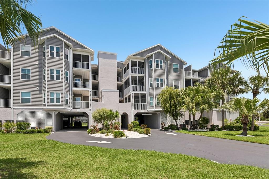 A multi-story apartment building with gray siding, screened balconies, and ground-level covered parking — 5727 BISCAYNE COURT UNIT 209, NEW PORT RICHEY, FL