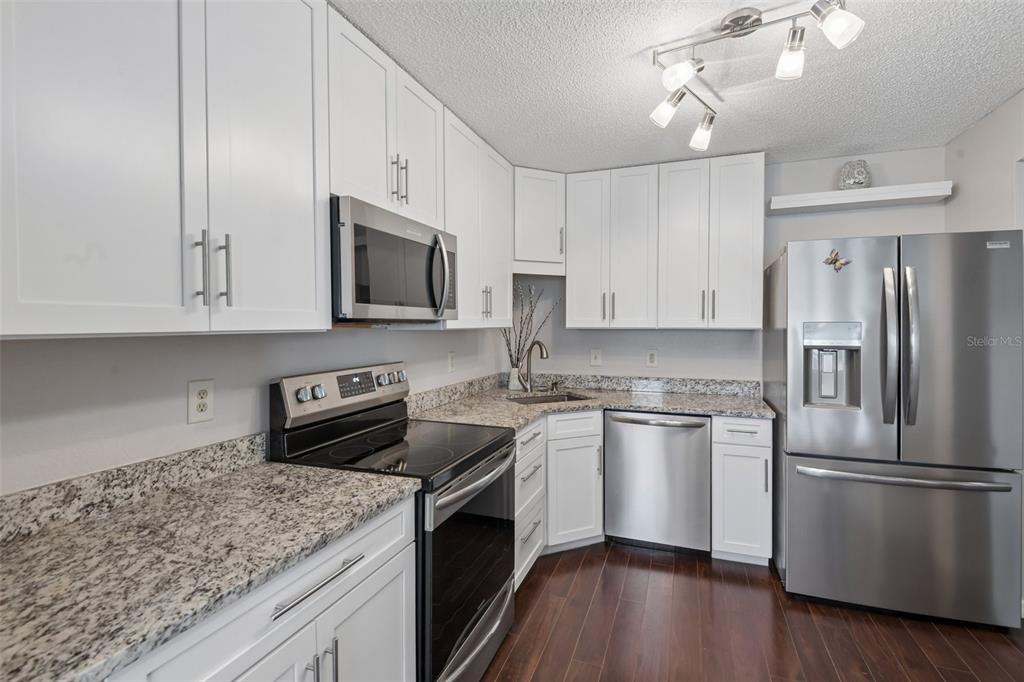 A kitchen features white cabinets, granite countertops, stainless steel appliances, and dark wood flooring — 5727 BISCAYNE COURT UNIT 209, NEW PORT RICHEY, FL
