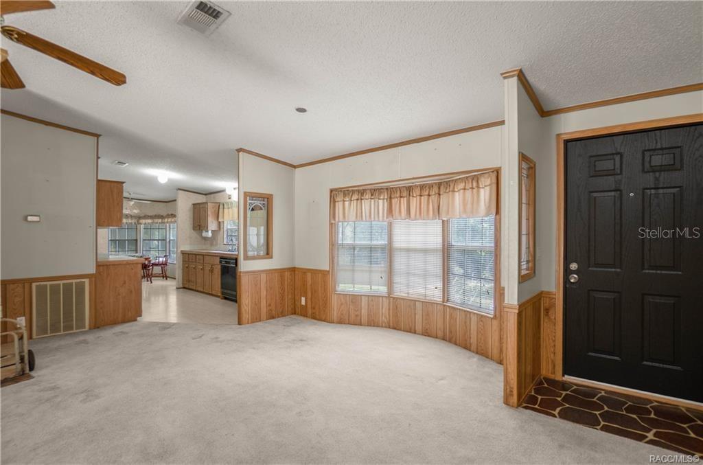 A living room with beige carpet, wood wainscoting, a bay window, and a black front door — 9300 CR 647A, BUSHNELL, FL