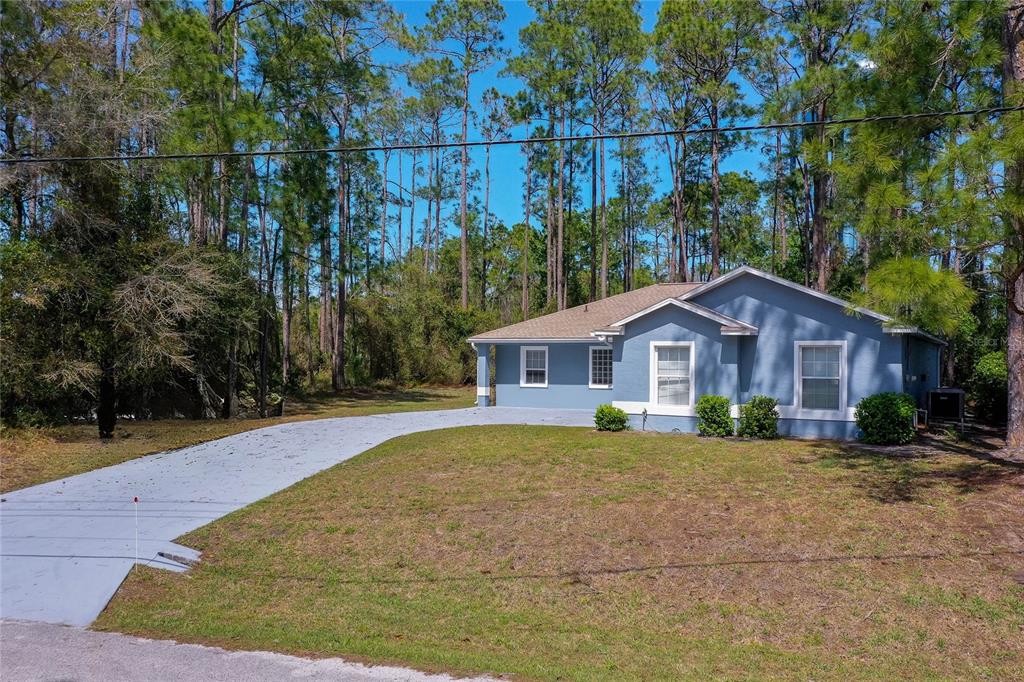 A blue single-story house with a paved driveway sits on a wooded lot — 7 PENINSULA LANE, PALM COAST, FL