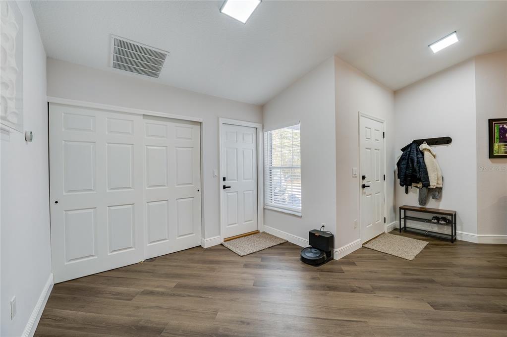 An entryway features wood-look flooring, white doors, a coat rack, and a robotic vacuum — 7 PENINSULA LANE, PALM COAST, FL