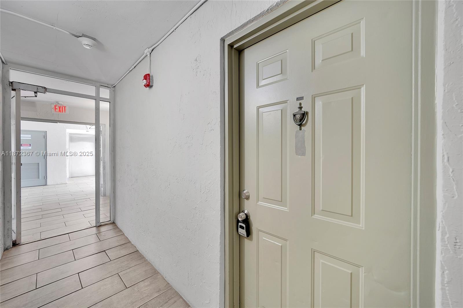 A light-colored door with a lockbox and knocker sits in a hallway with tiled floors — 8260 SW 210th St # 201, Cutler Bay FL 33189, CUTLER BAY, FL