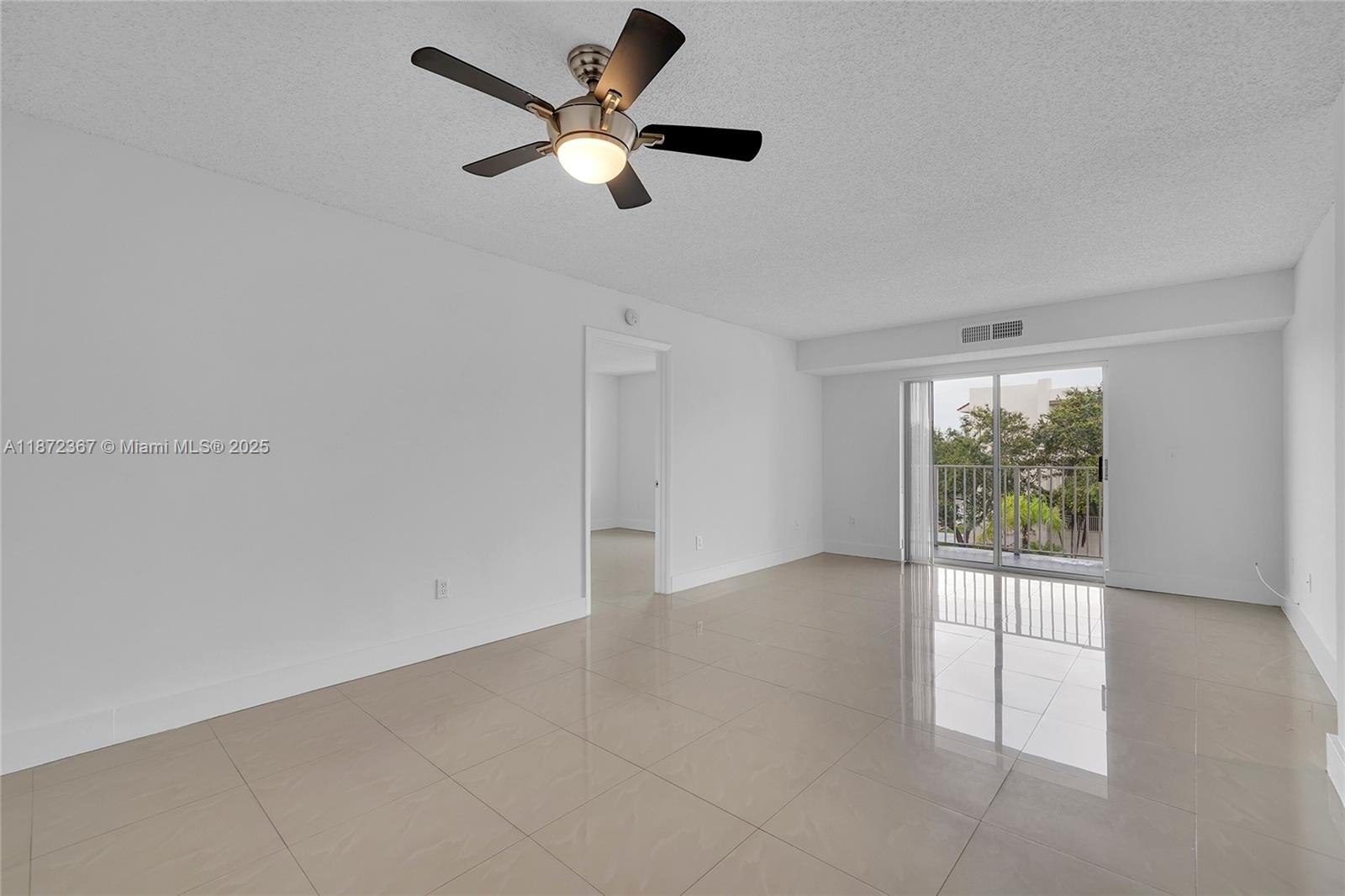 An empty room features white walls, light tile flooring, a ceiling fan, and a balcony — 8260 SW 210th St # 201, Cutler Bay FL 33189, CUTLER BAY, FL