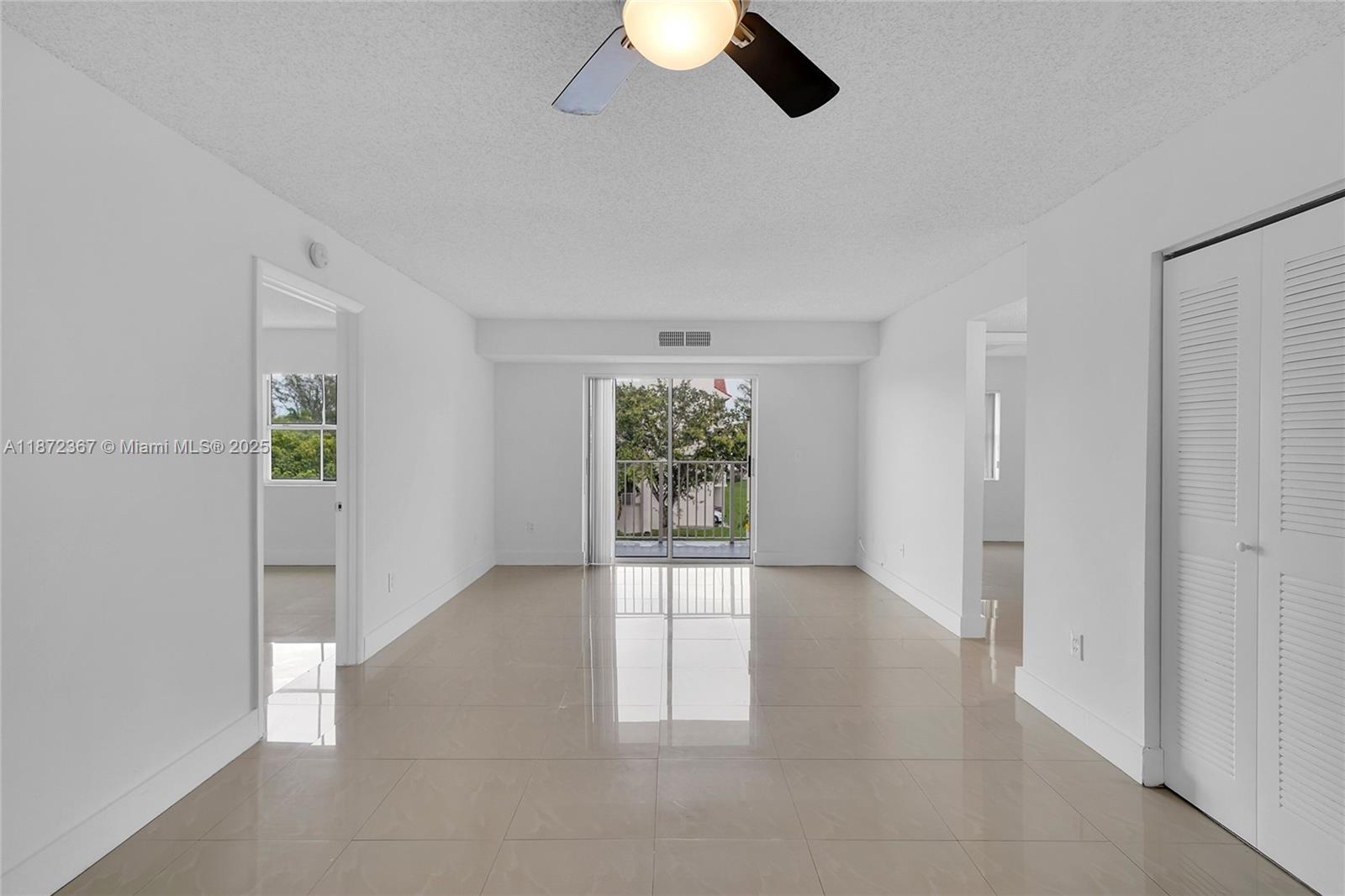 A bright, empty living room features white walls, beige tile floors, and a balcony view — 8260 SW 210th St # 201, Cutler Bay FL 33189, CUTLER BAY, FL