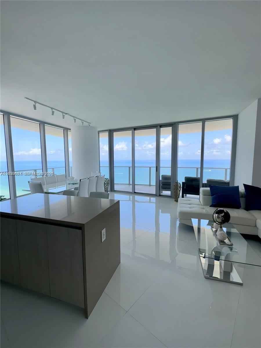 A modern living and dining area features white tile floors, floor-to-ceiling windows, and ocean views — 4111 S Ocean Dr # 2902, Hollywood FL 33019, HOLLYWOOD, FL