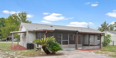 The exterior of a single-story house features a screened-in porch and a metal carport — 35904 DAWN DRIVE, LEESBURG, FL