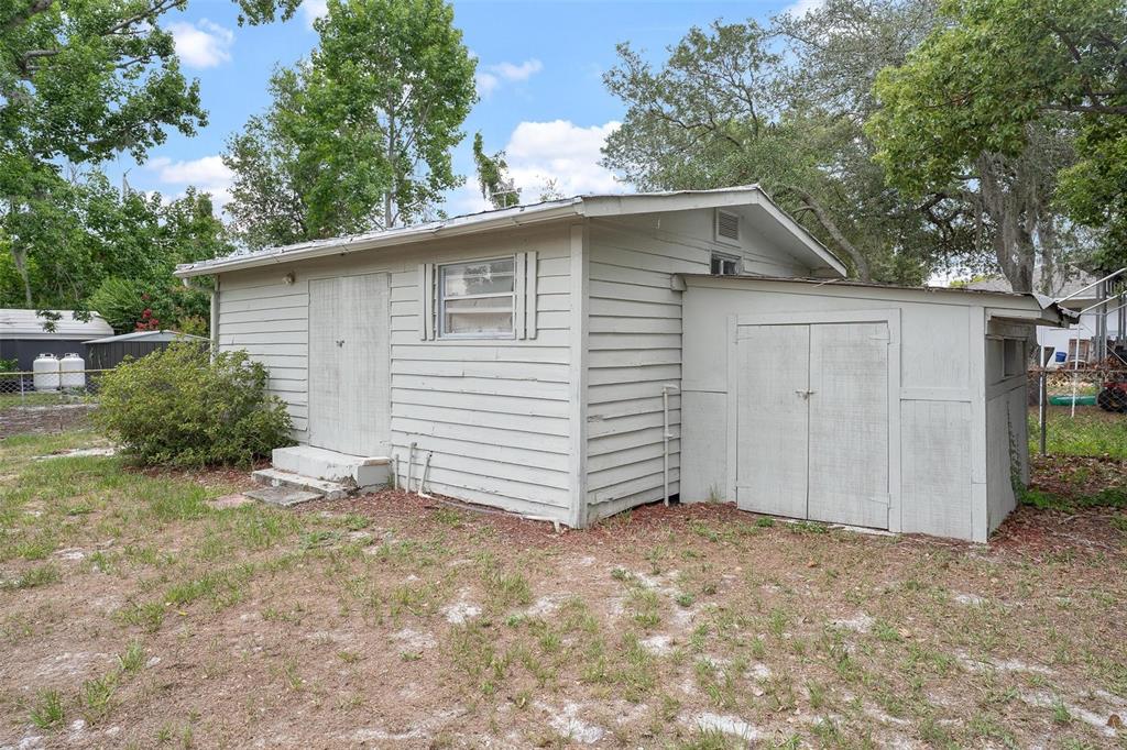 A light-colored, wood-sided shed with a double-door entrance and an attached storage lean-to — 35904 DAWN DRIVE, LEESBURG, FL