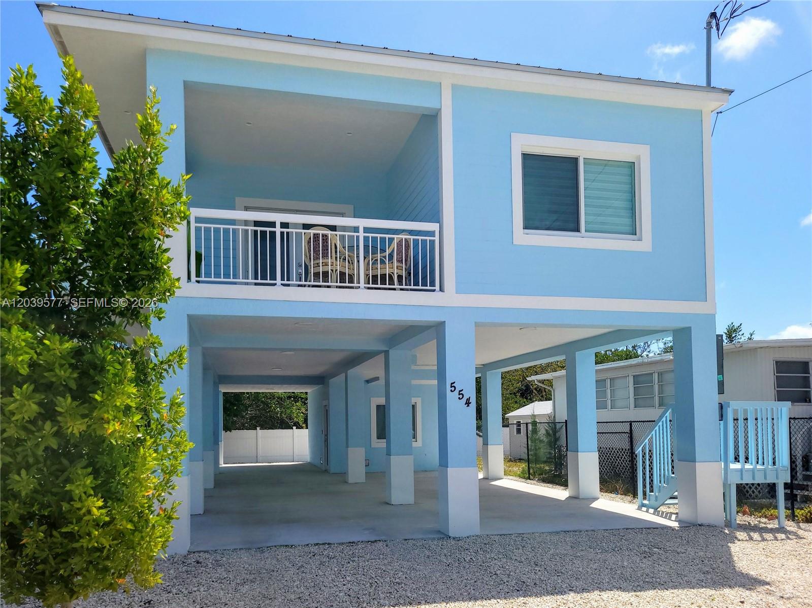 A light blue, two-story stilt house features a covered ground-level parking area and a balcony — 554 Gordon Cir, Key Largo FL 33037, KEY LARGO, FL