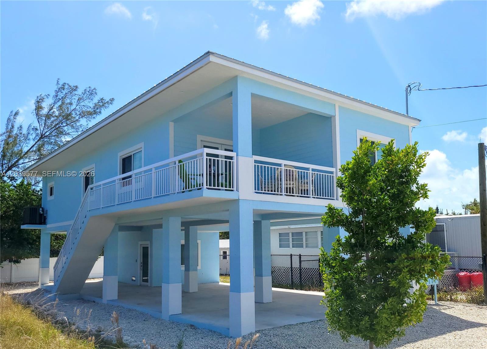 A light blue elevated house features a wrap-around balcony and an open ground-level carport — 554 Gordon Cir, Key Largo FL 33037, KEY LARGO, FL