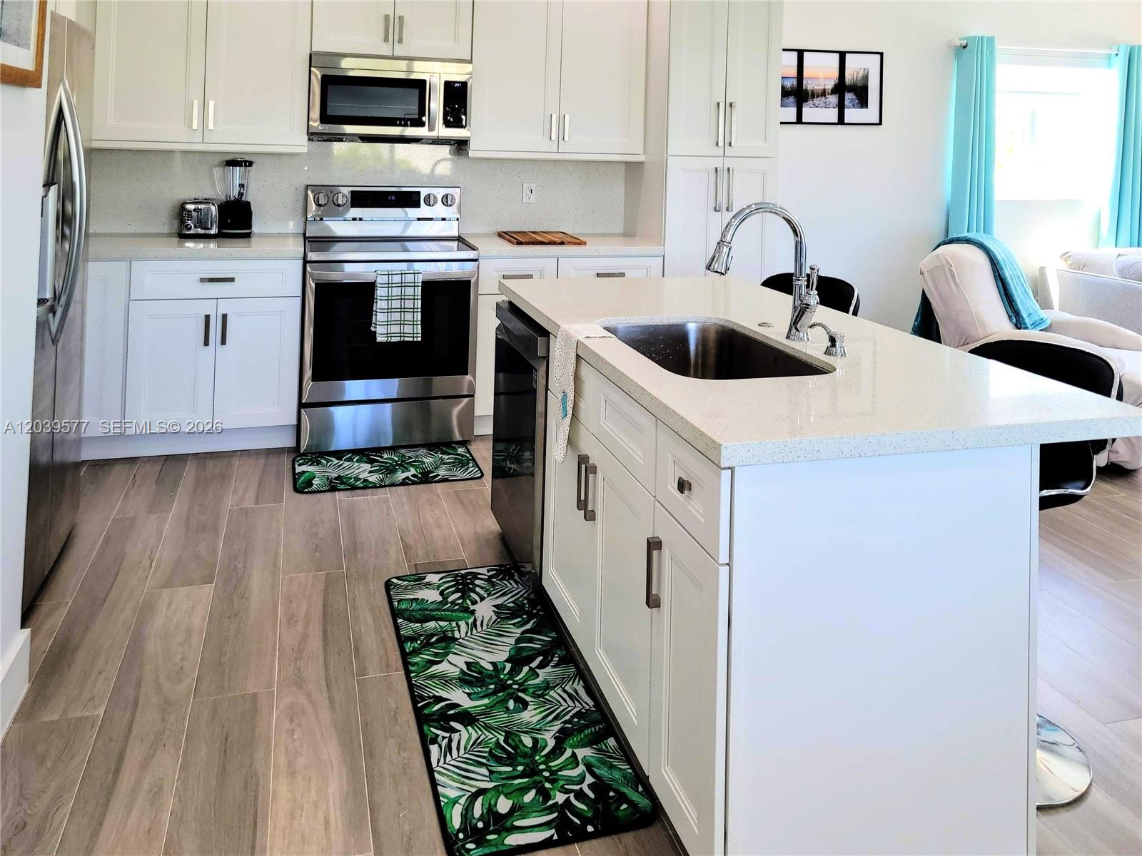 A modern kitchen features white cabinets, stainless steel appliances, a center island, and wood-look flooring — 554 Gordon Cir, Key Largo FL 33037, KEY LARGO, FL