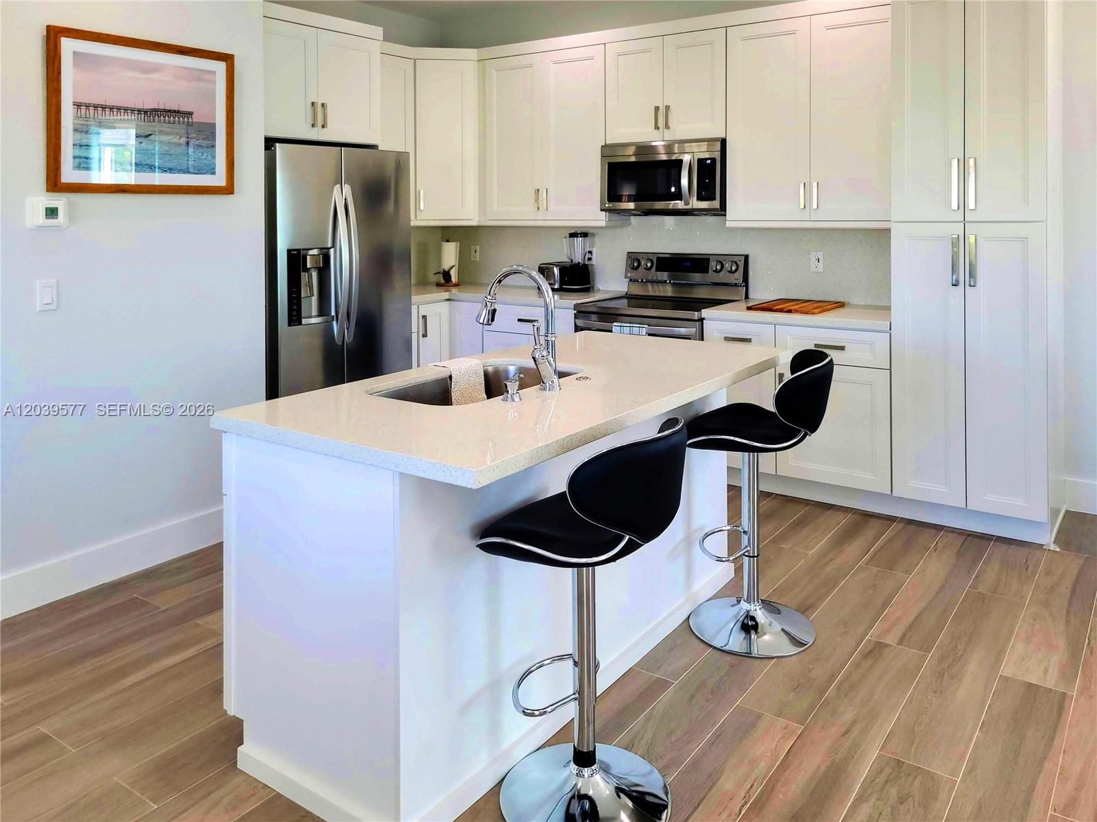 A modern kitchen features white cabinets, stainless steel appliances, a quartz island, and bar stools — 554 Gordon Cir, Key Largo FL 33037, KEY LARGO, FL