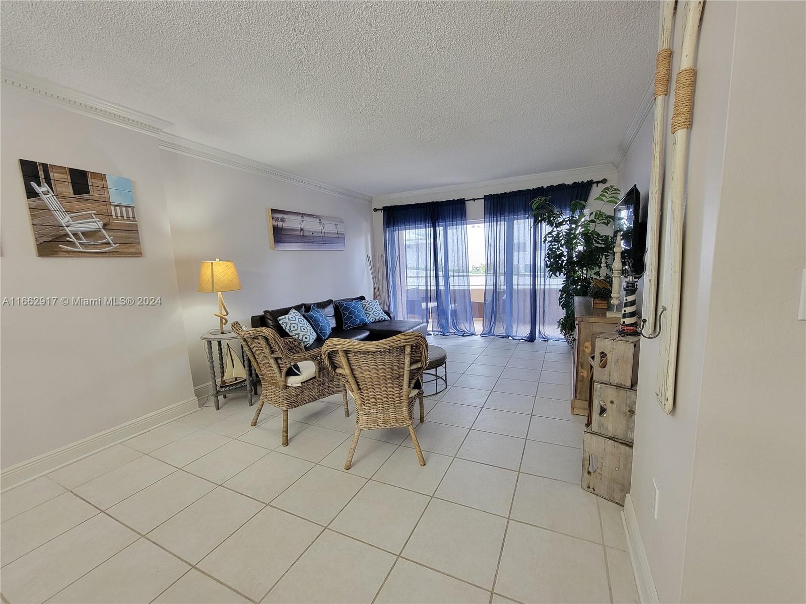A living room features tile flooring, wicker chairs, a dark sofa, and blue curtains — 1980 S Ocean Dr # 2C, Hallandale Beach FL 33009, HALLANDALE BEACH, FL