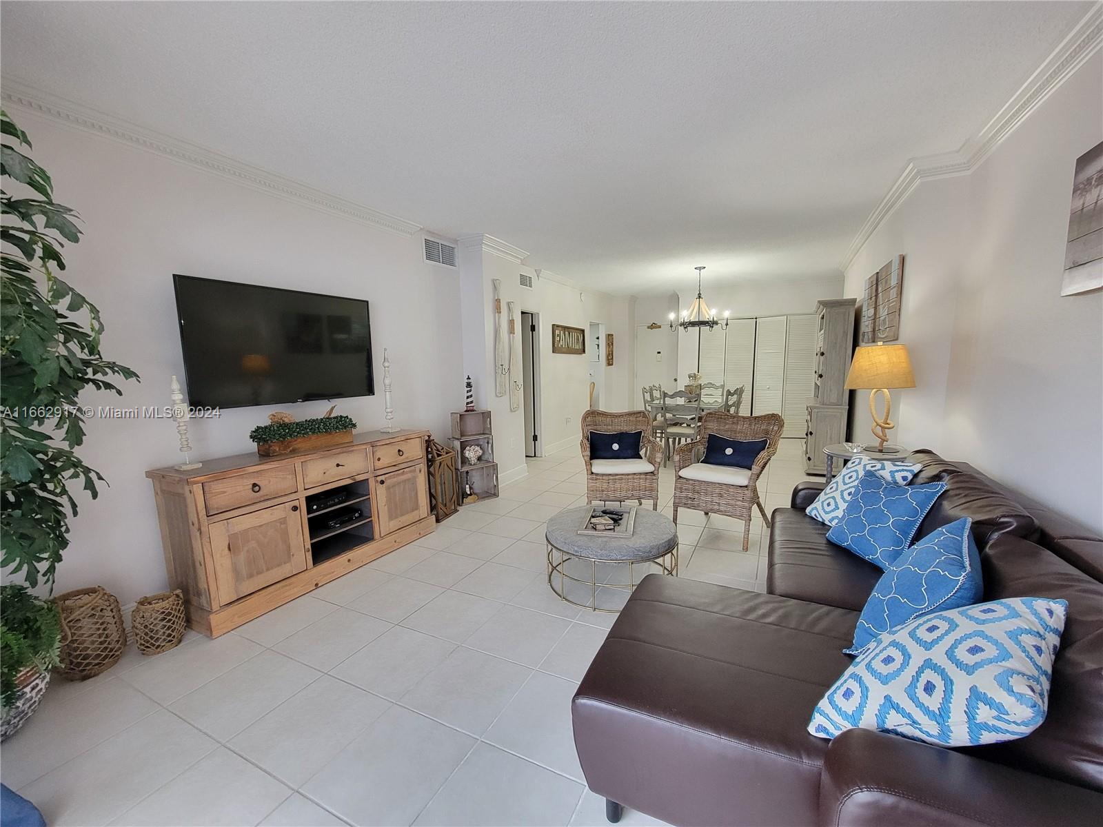 A living room features a brown leather sectional, wicker chairs, and a wooden media console — 1980 S Ocean Dr # 2C, Hallandale Beach FL 33009, HALLANDALE BEACH, FL