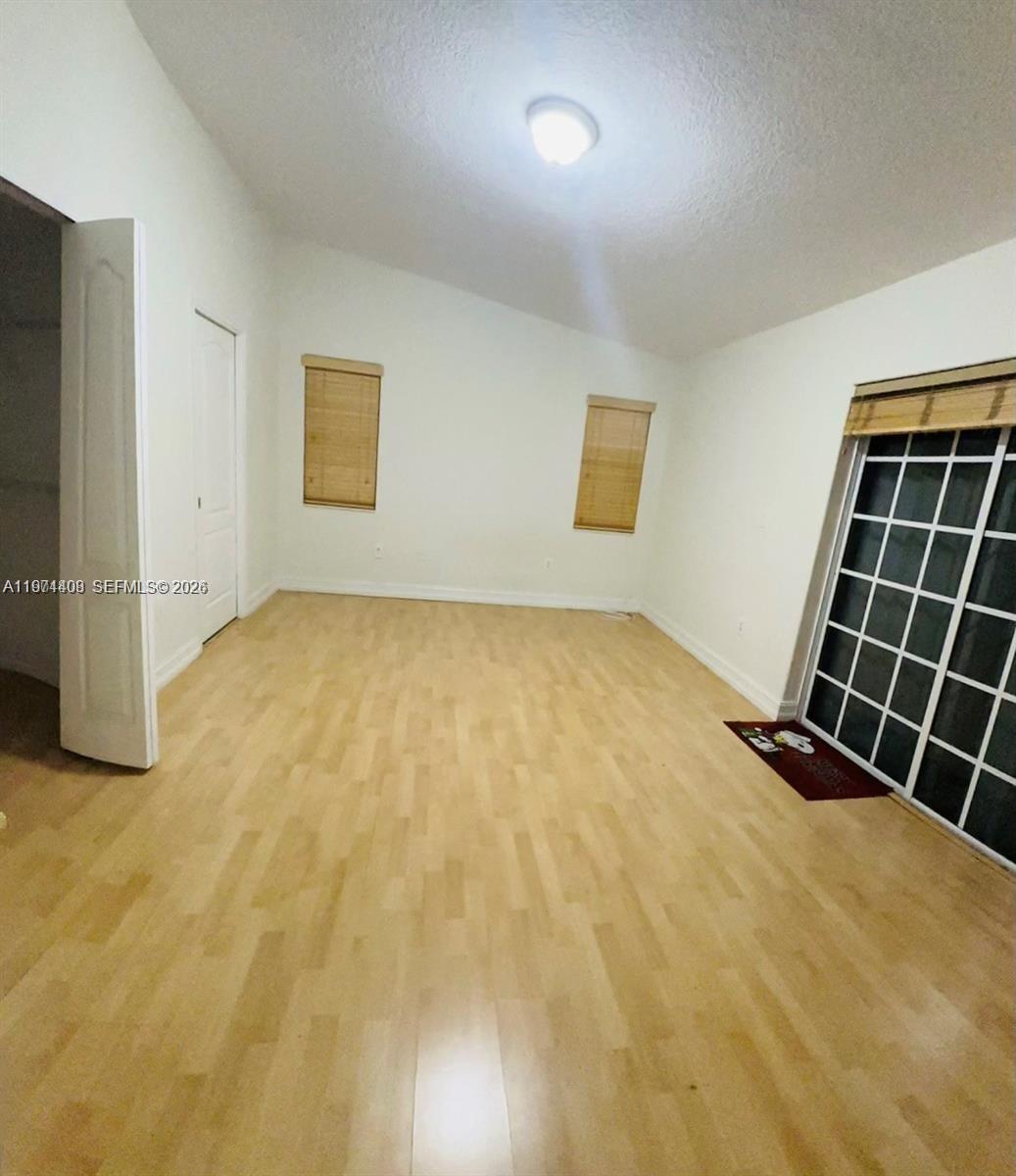 An empty room features light wood flooring, white walls, two windows, and a sliding glass door — 87** NW 150th Ter # 0, Miami Lakes FL 33018, MIAMI LAKES, FL