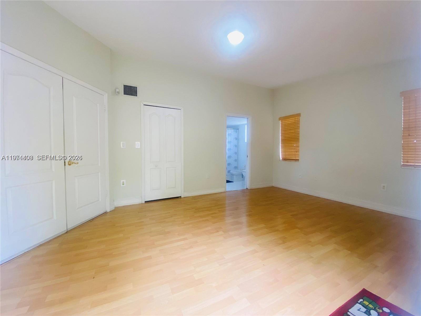 An empty bedroom features light wood flooring, white walls, two closets, and an attached bathroom — 87** NW 150th Ter # 0, Miami Lakes FL 33018, MIAMI LAKES, FL