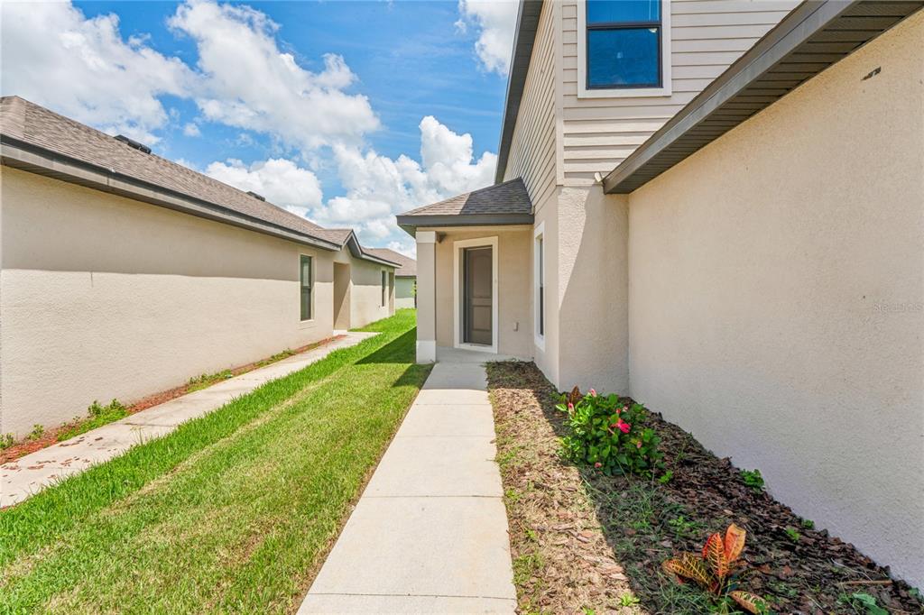 A concrete walkway leads to a side entrance between two beige stucco houses — 2427 CASPIAN DRIVE, LAKELAND, FL