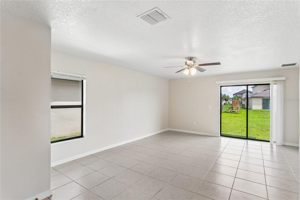 An empty living room with light tile flooring, a ceiling fan, and sliding glass doors — 2427 CASPIAN DRIVE, LAKELAND, FL