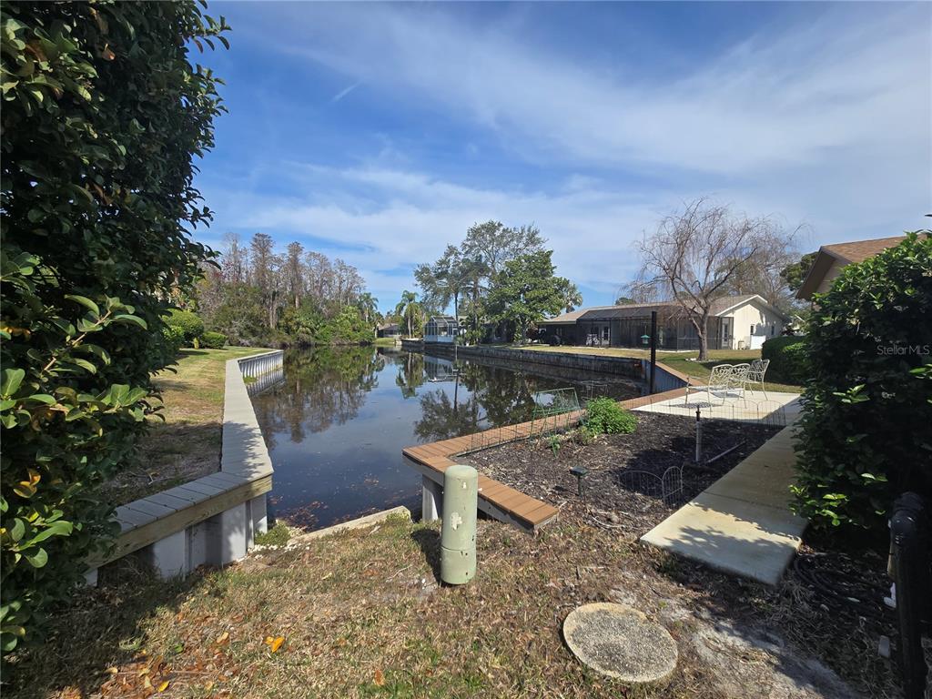 A backyard view features a canal with a wooden bulkhead and a small garden bed — 300 CYPRESS CREEK CIRCLE, OLDSMAR, FL