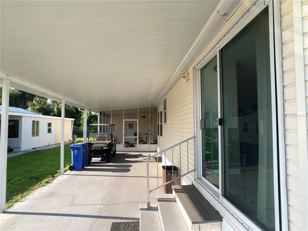 A covered concrete carport area with a golf cart, trash bins, and sliding glass doors — 1710 7TH STREET SW UNIT 85, RUSKIN, FL