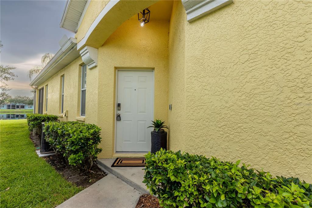 A yellow stucco house exterior features a white front door, a walkway, and green landscaping — 11447 CAPTIVA KAY DRIVE, RIVERVIEW, FL