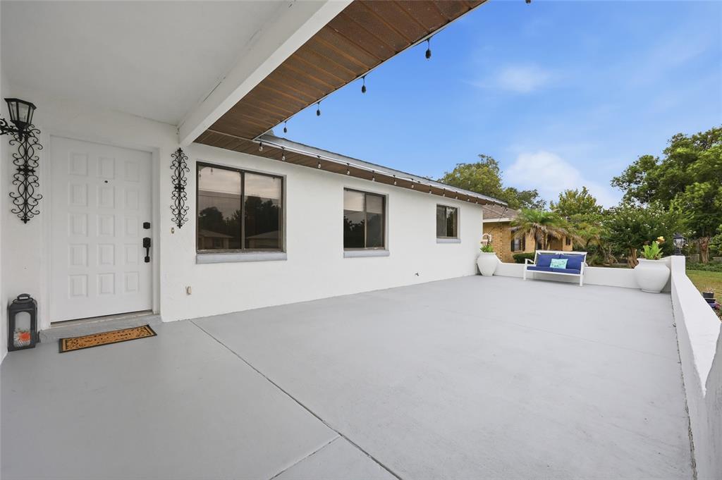 A white house exterior features a large gray concrete patio, a front door, and windows — 1025 PARK AVENUE, TAVARES, FL