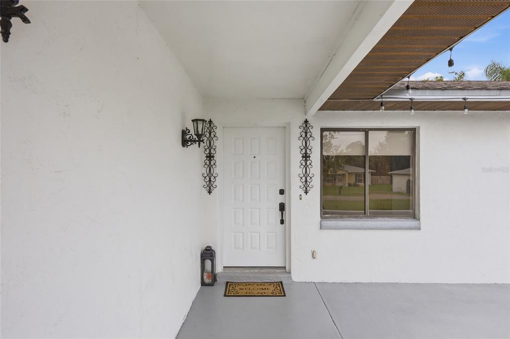 A white front door with decorative metal accents sits under a covered porch entryway — 1025 PARK AVENUE, TAVARES, FL