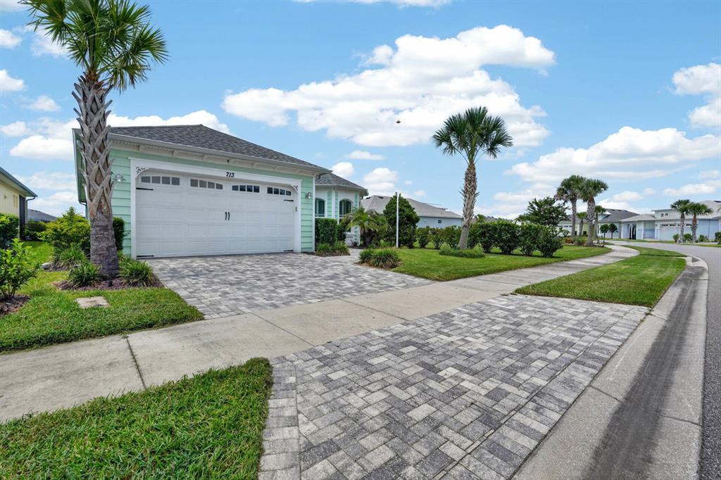 A light green house with a paver driveway and palm trees under a cloudy sky — 713 LANDSHARK BOULEVARD, DAYTONA BEACH, FL