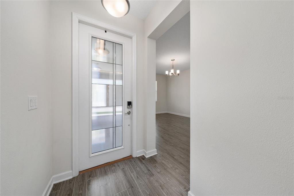 A white front door with a glass panel opens into a foyer with wood-look flooring — 12066 GRAMMAR LANE, ORLANDO, FL