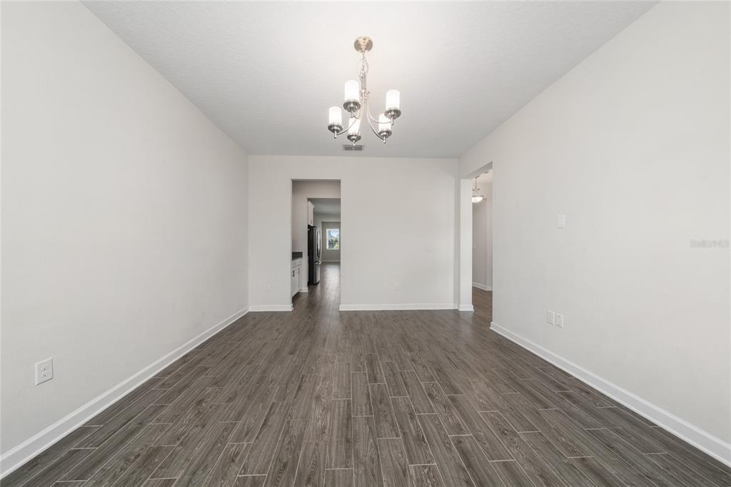 A dining room with gray wood-look flooring, white walls, and a modern chandelier — 12066 GRAMMAR LANE, ORLANDO, FL