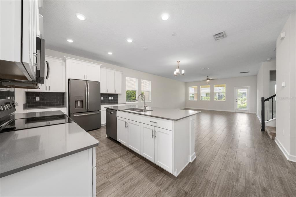 A modern kitchen with white cabinets, a central island, and stainless steel appliances opens to a living area — 12066 GRAMMAR LANE, ORLANDO, FL