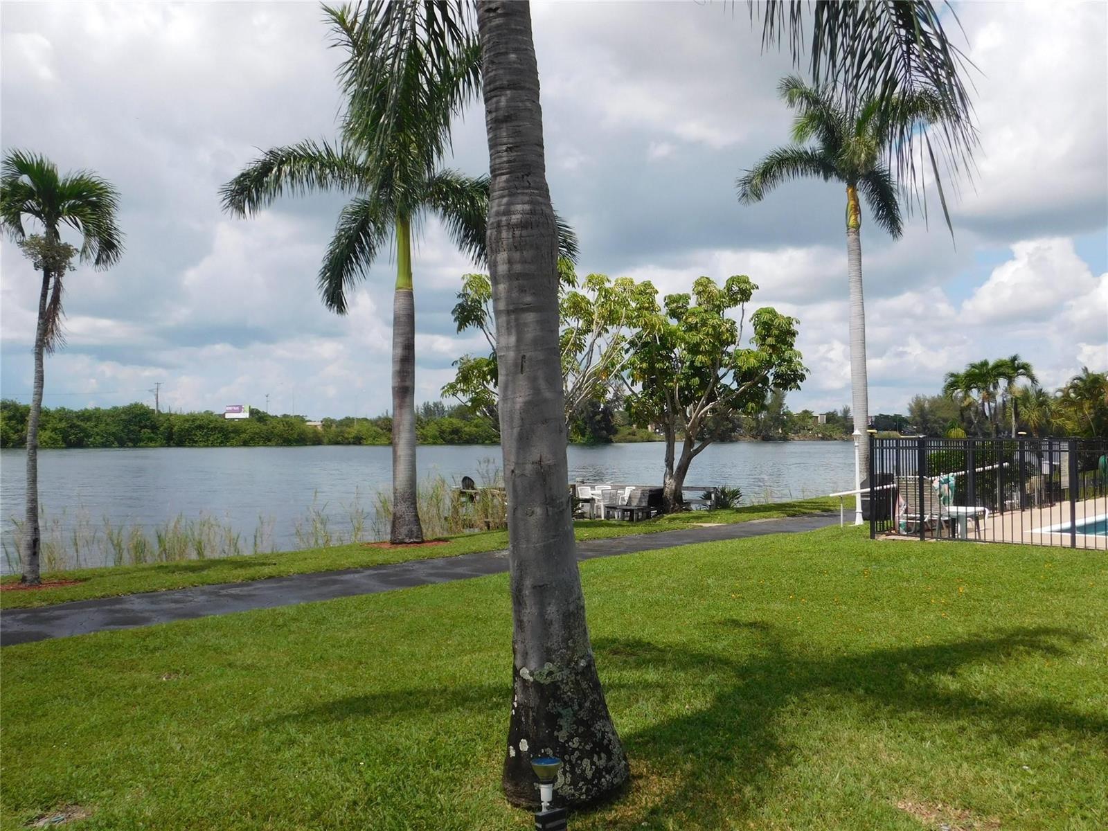 A grassy lawn with palm trees overlooks a lake near a fenced pool area — 960 Crystal Lake Drive # 201, Deerfield Beach FL 33064, DEERFIELD BEACH, FL