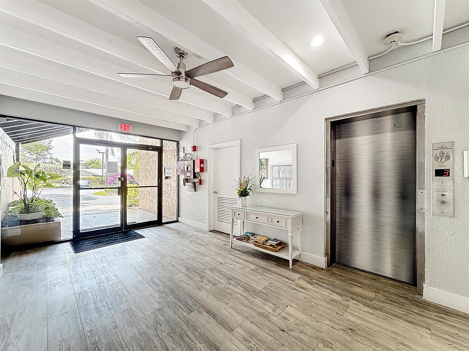 A building lobby features wood-look flooring, a ceiling fan, a white console table, and an elevator — 755 Dotterel Road # 1411, Delray Beach FL 33444, DELRAY BEACH, FL