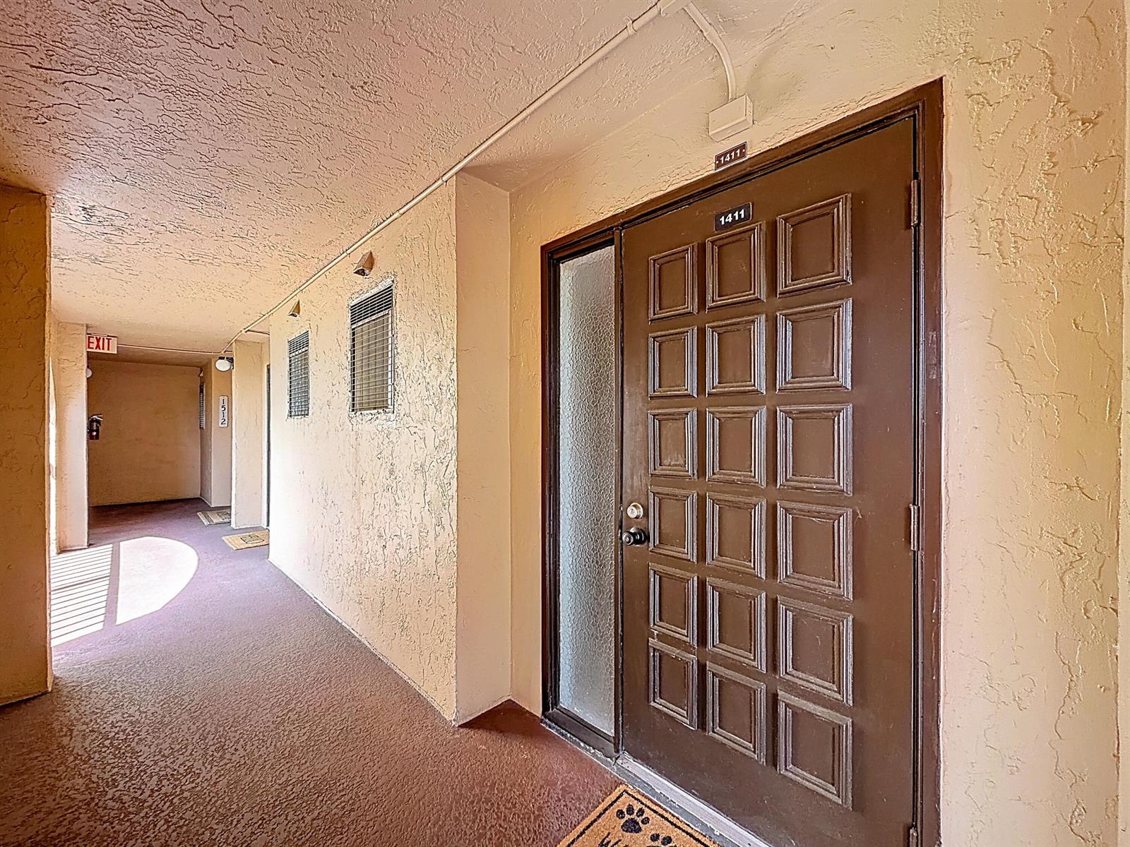 A brown door with a side window is located in a beige apartment building hallway — 755 Dotterel Road # 1411, Delray Beach FL 33444, DELRAY BEACH, FL
