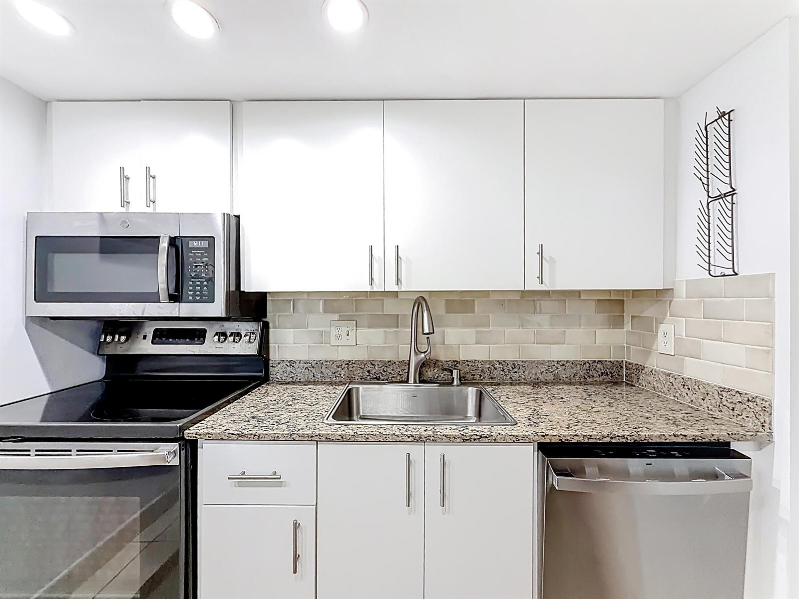 A kitchen features white cabinets, granite countertops, a stainless steel sink, and stainless steel appliances — 755 Dotterel Road # 1411, Delray Beach FL 33444, DELRAY BEACH, FL