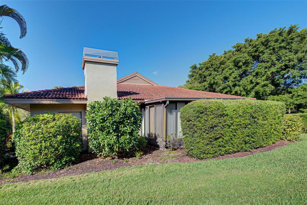 A single-story house with a tiled roof, chimney, and large hedges in a grassy yard — 1740 LANDINGS BOULEVARD UNIT 39, SARASOTA, FL