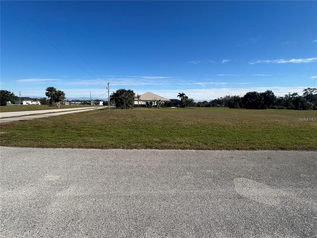 A vacant, grassy lot sits along a paved road under a clear blue sky — 16447 AYSON WAY, PUNTA GORDA, FL