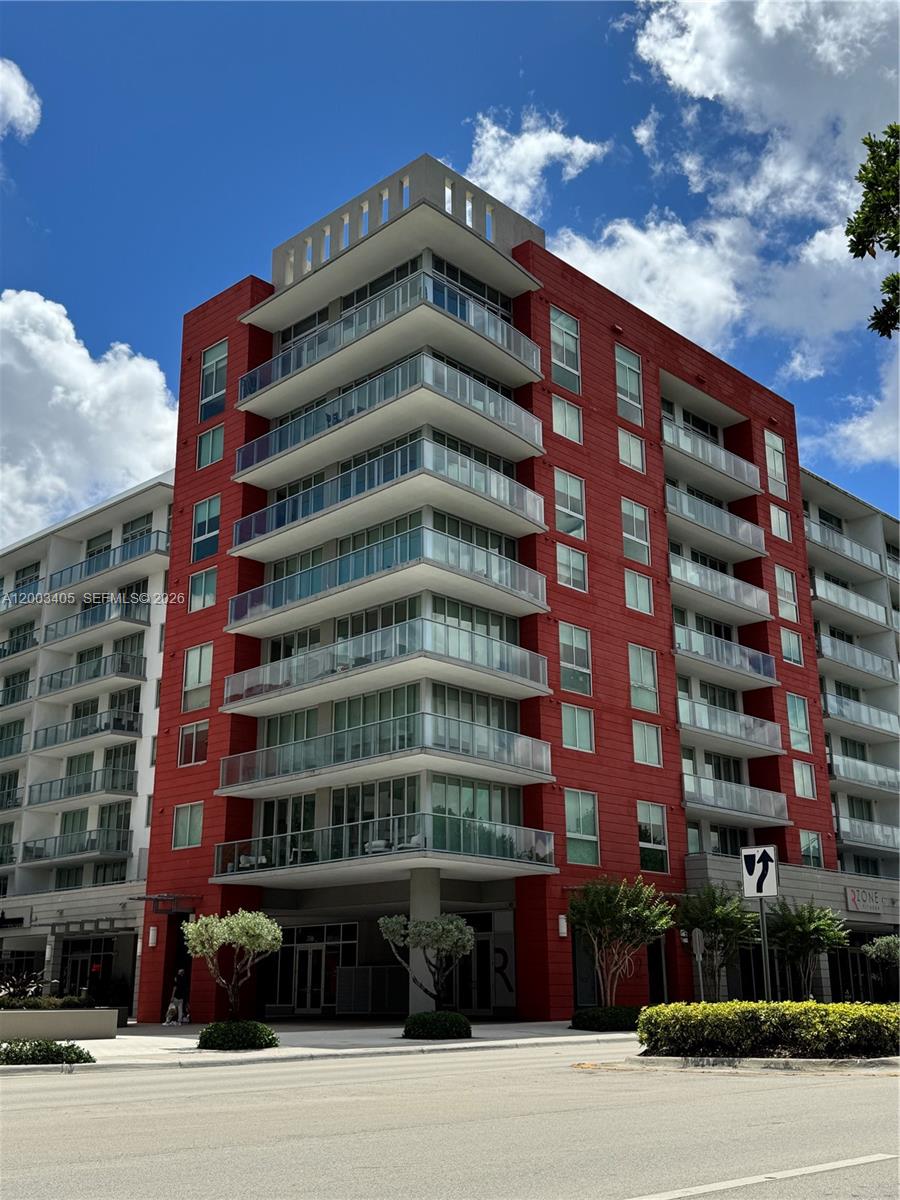 A multi-story building features a red facade with wrap-around glass balconies and ground-level storefronts — 7751 NW 107th Ave # 411, Doral FL 33178, DORAL, FL