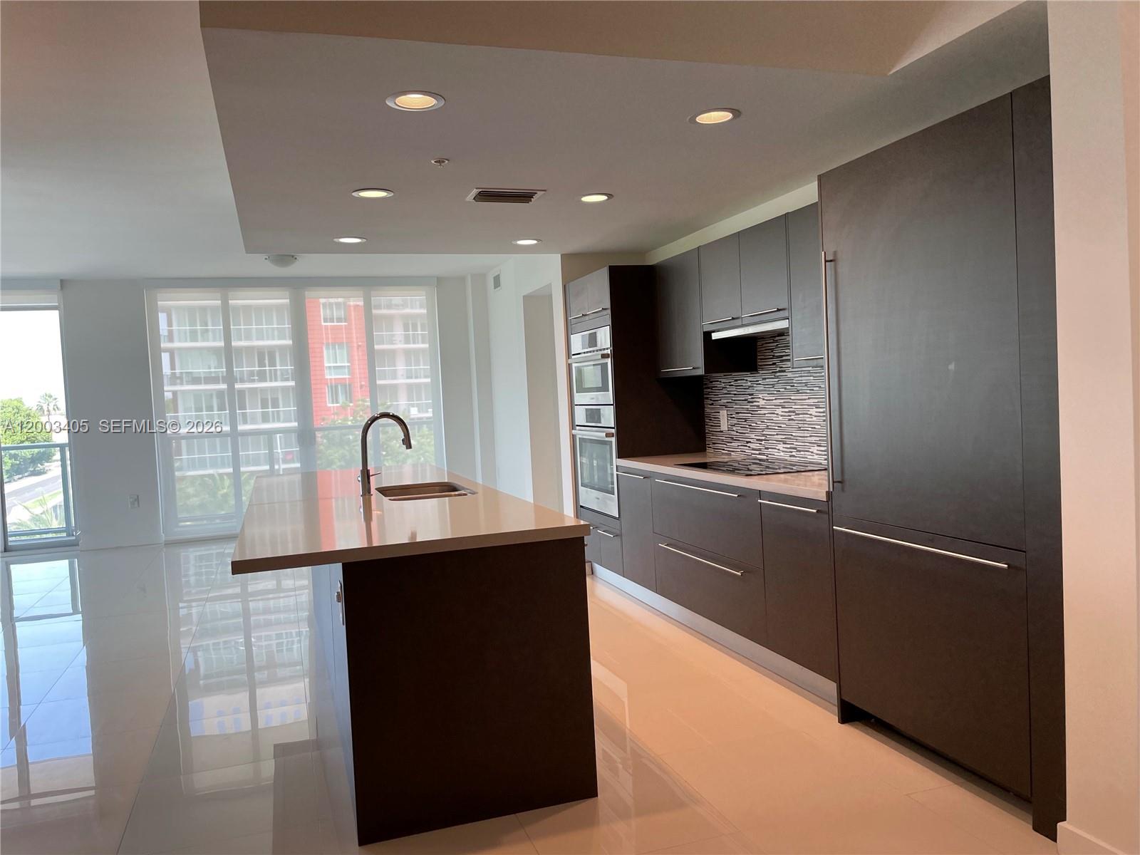 A modern kitchen features dark cabinetry, a central island with a sink, and tile flooring — 7751 NW 107th Ave # 411, Doral FL 33178, DORAL, FL