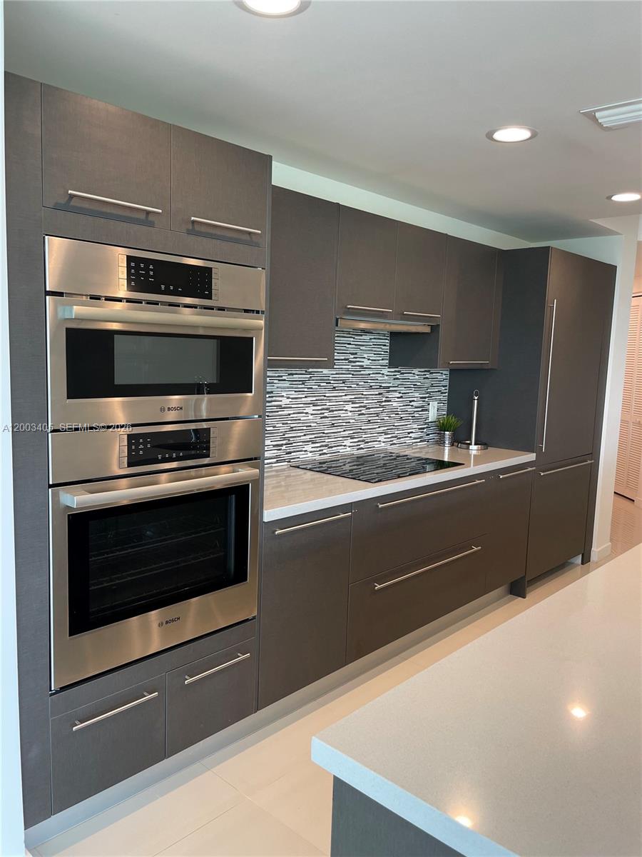 A modern kitchen features dark gray cabinetry, stainless steel Bosch appliances, and a tiled backsplash — 7751 NW 107th Ave # 411, Doral FL 33178, DORAL, FL