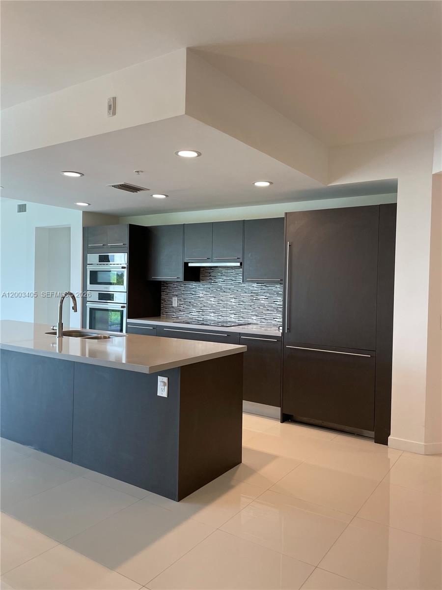A modern kitchen features dark cabinetry, a large island with a sink, and light flooring — 7751 NW 107th Ave # 411, Doral FL 33178, DORAL, FL