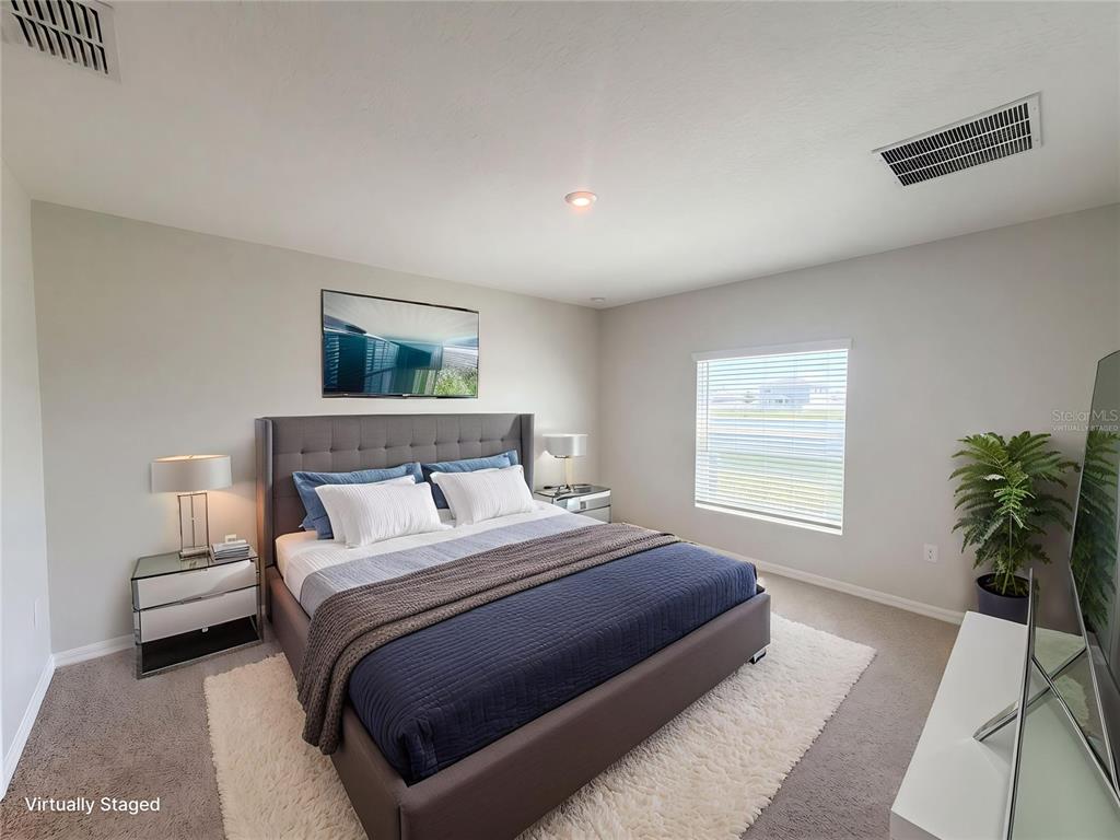 A bedroom features a gray upholstered bed, two nightstands, a window, and a potted plant — 221 AQUAMARINE LANE, KISSIMMEE, FL