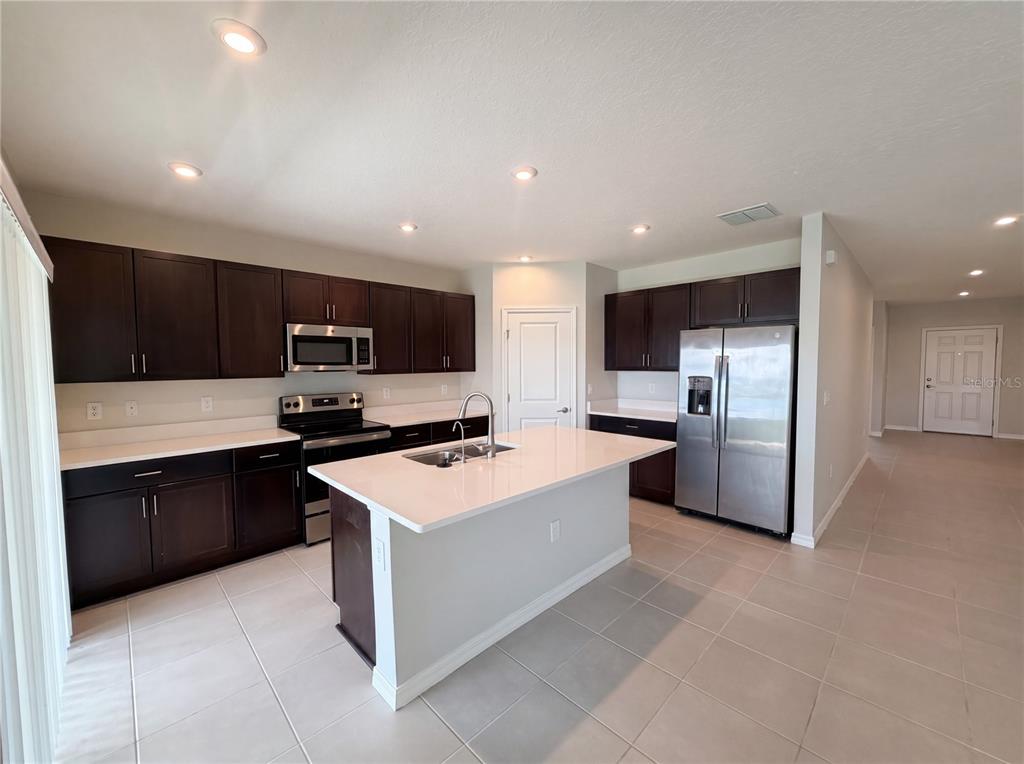 A kitchen with dark wood cabinets, white countertops, a central island, and stainless steel appliances — 221 AQUAMARINE LANE, KISSIMMEE, FL