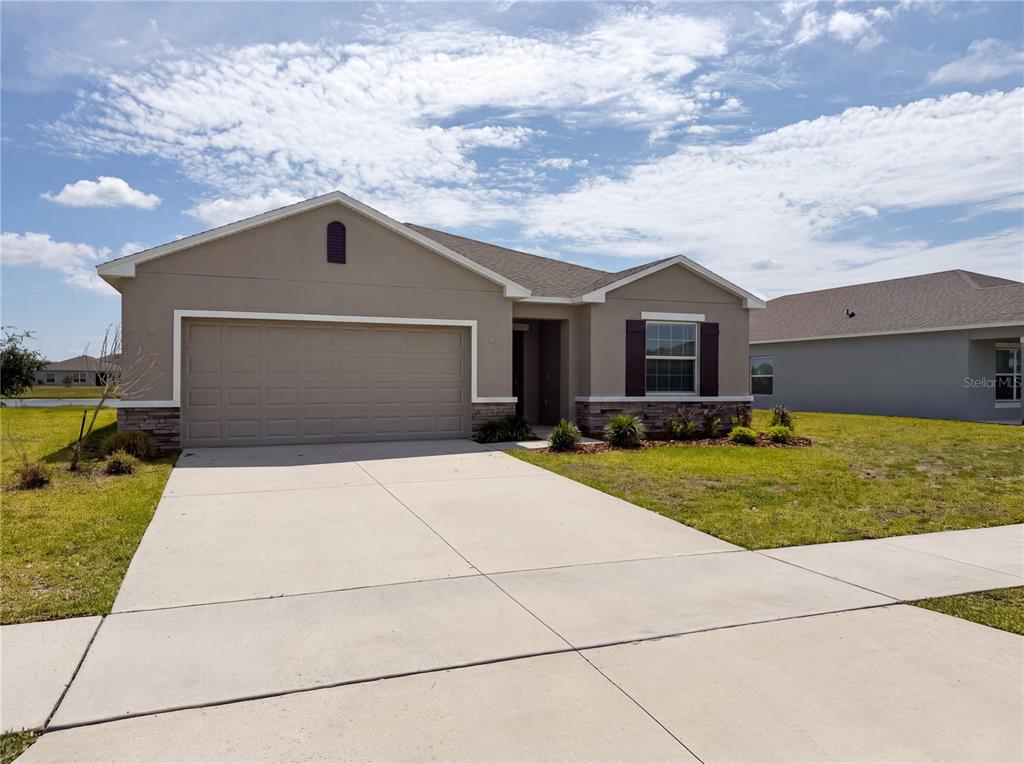 A single-story house with a two-car garage, tan stucco siding, and a concrete driveway — 221 AQUAMARINE LANE, KISSIMMEE, FL