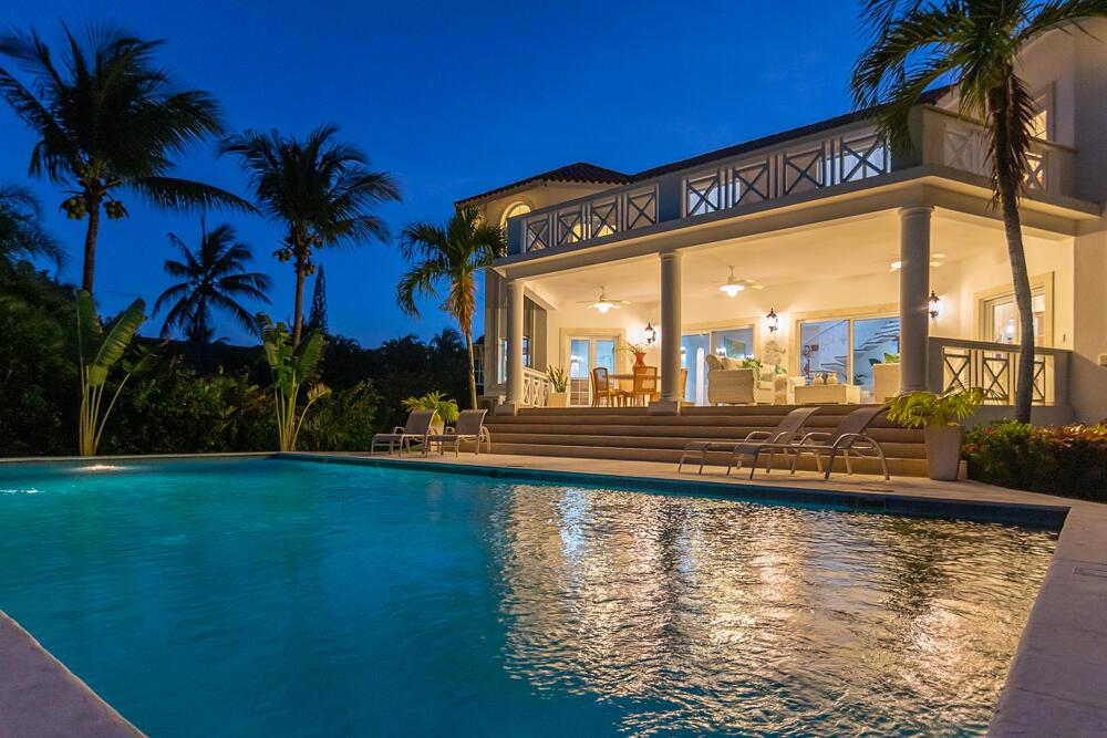 A swimming pool sits in front of a two-story house with a lit covered patio — 123 Villa Cabarete, FL