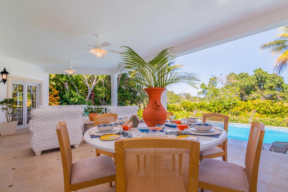 A covered outdoor dining patio features a round table, wicker chairs, and a swimming pool — 123 Villa Cabarete, FL