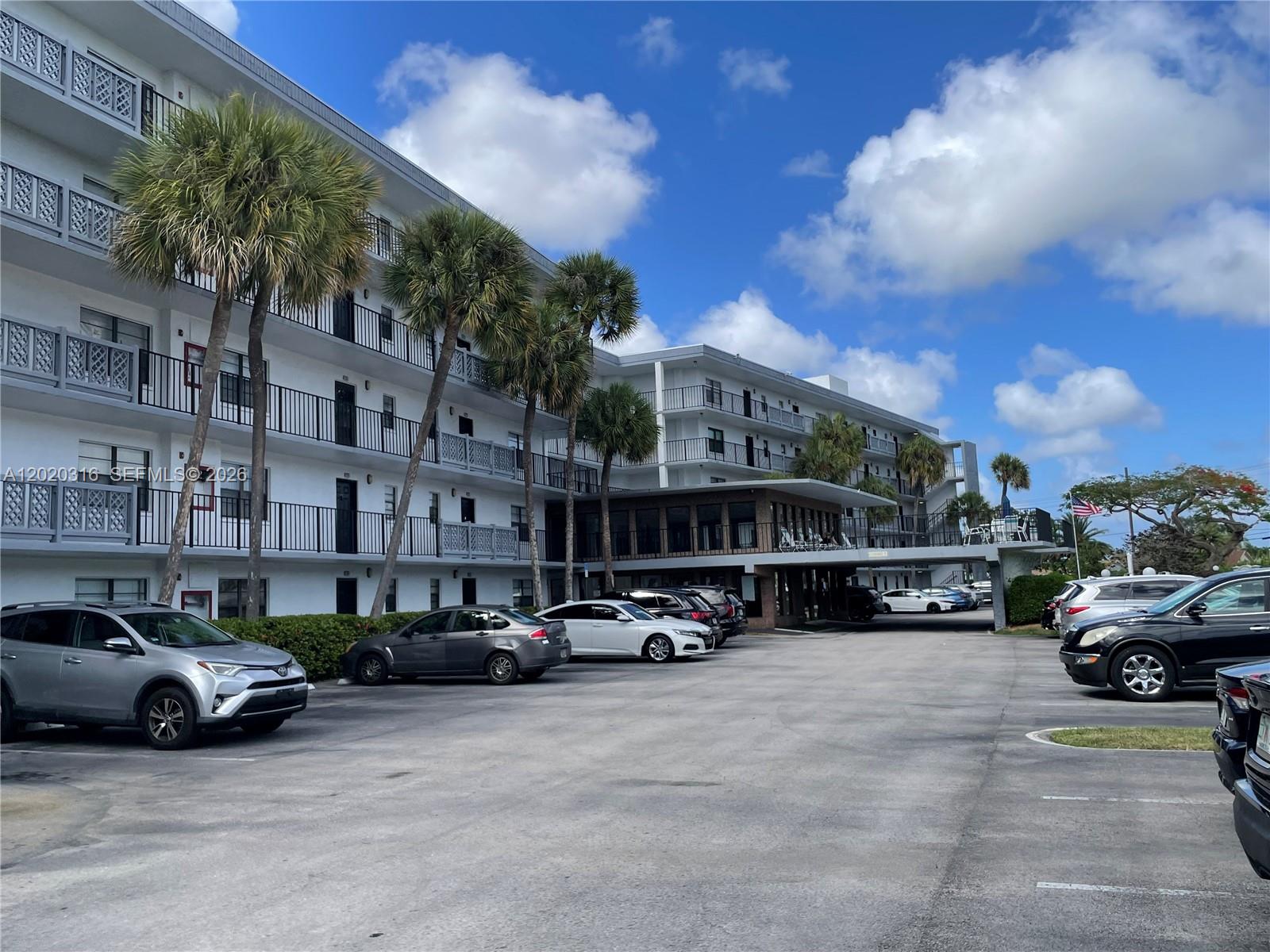 A multi-story apartment building with palm trees and a parking lot in the foreground — 9235 SW 8th St # 209, Boca Raton FL 33428, BOCA RATON, FL