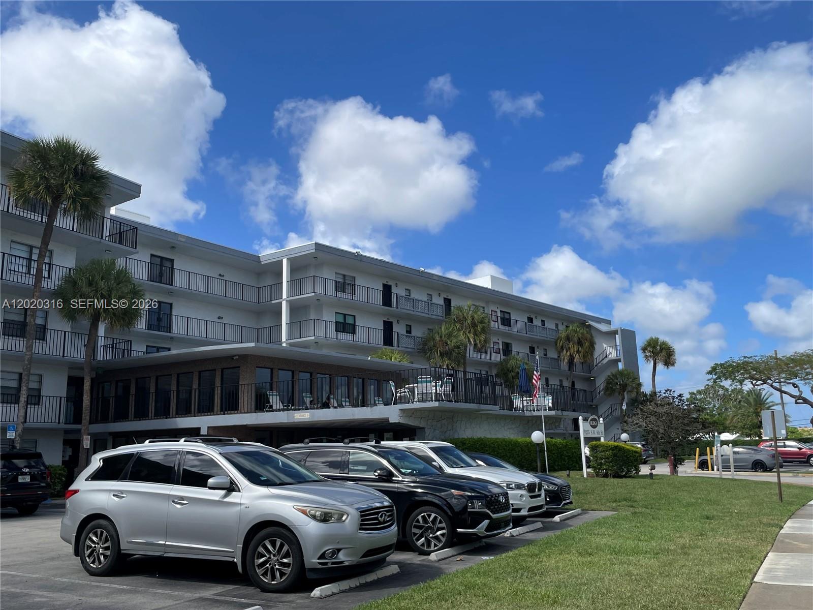 A multi-story apartment building with balconies stands behind a parking lot with several cars — 9235 SW 8th St # 209, Boca Raton FL 33428, BOCA RATON, FL