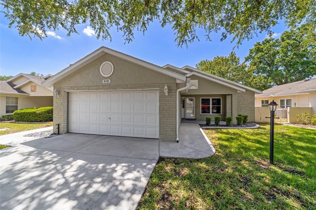 A single-story house with a beige brick facade, a two-car garage, and a concrete walkway — 9181 SW 91ST CIRCLE, OCALA, FL