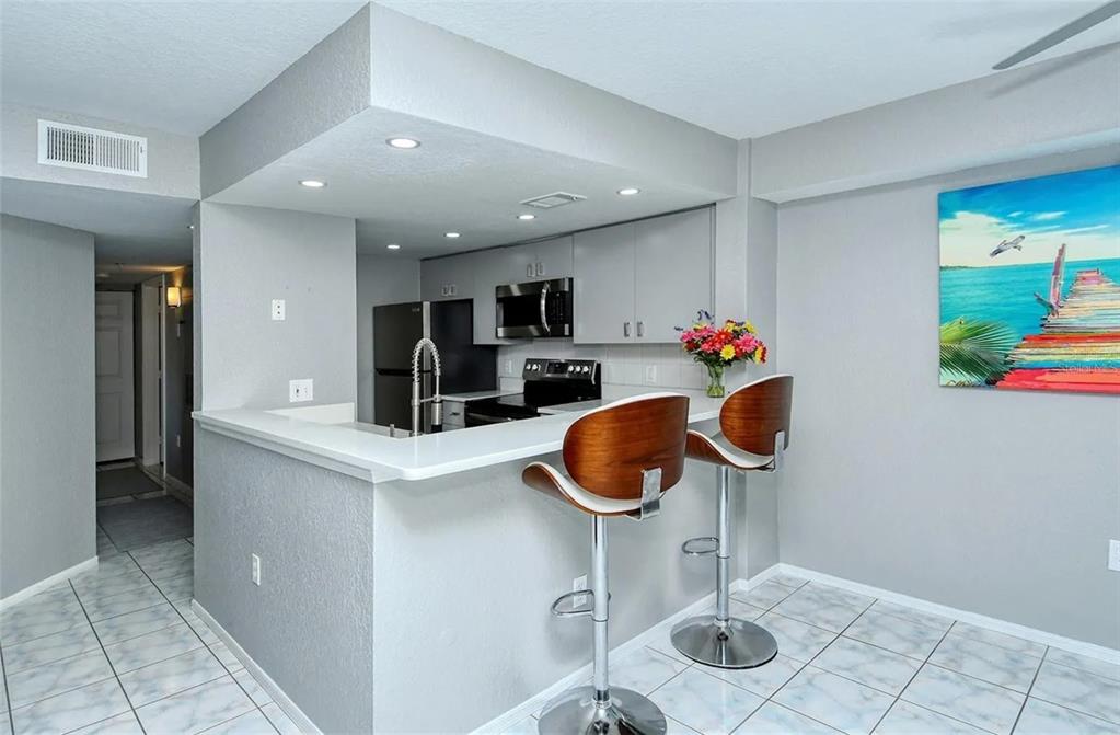 A kitchen with gray cabinets, white countertops, and two bar stools at a breakfast counter — 850 S TAMIAMI TRAIL UNIT 801, SARASOTA, FL